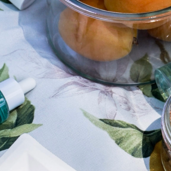 skincare serum and face mist on picnic blanket alongside some summer snacks