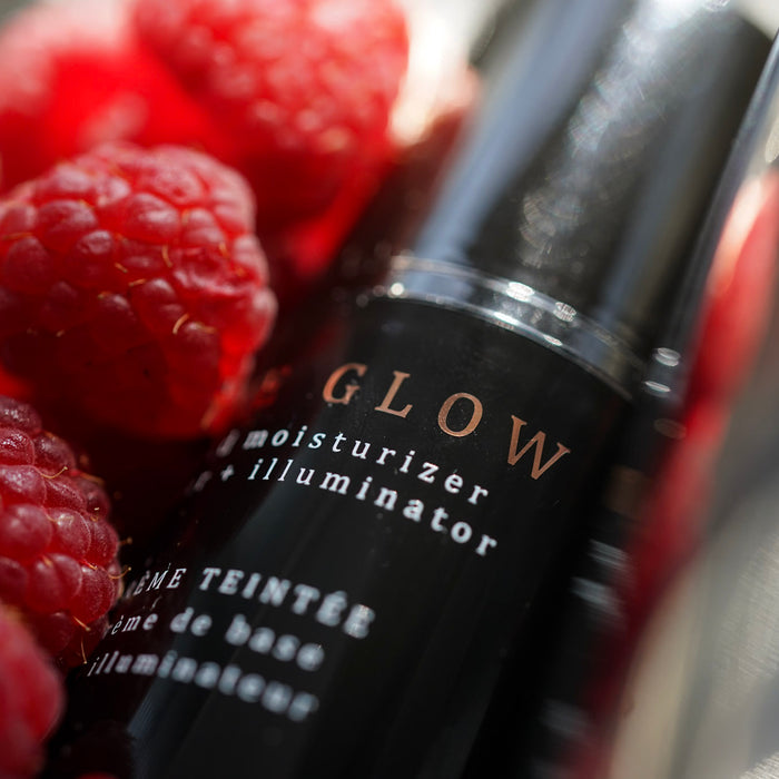 Raspberries in a wooden bowl with an amber glass bottle of raspberry seed oil surrounded by raspberries