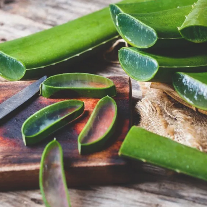 Slices of aloe vera on a wooden cutting board on a wooden table top.