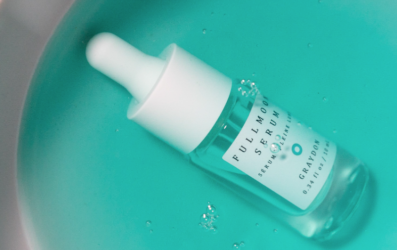 Bottle of Graydon Skincare Fullmoon Serum submerged in a lovely light blue bath of Fullmoon Serum.