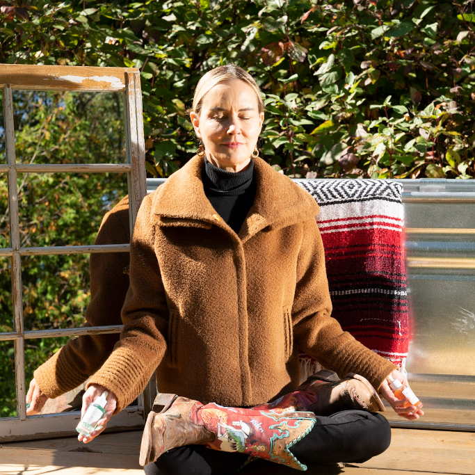 Graydon Moffat, meditating outdoors while holding a bottle of Graydon Skincare Fullmoon Serum and Graydon Skincare Moon Boost Serum.u