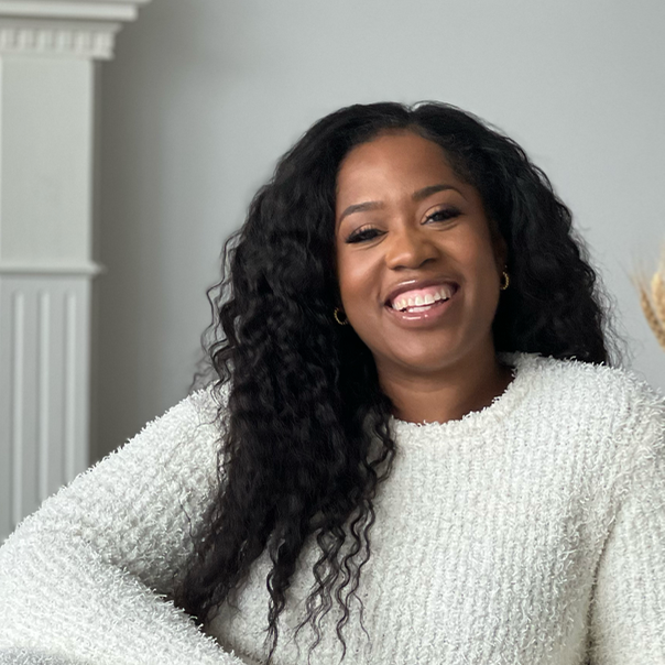 A smiling Jhanelle Peters sitting sideways on a couch, holding a camera