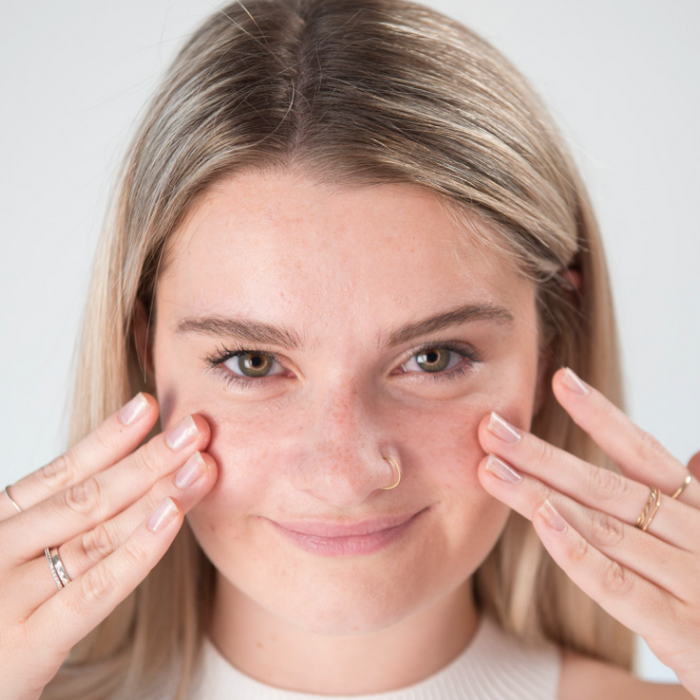 Young blonde woman with glowing skin touching her cheeks