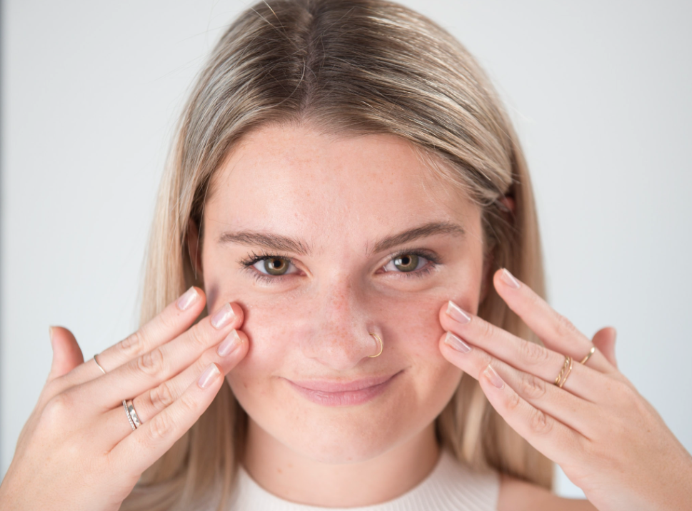 Young blonde woman with glowing skin touching her cheeks