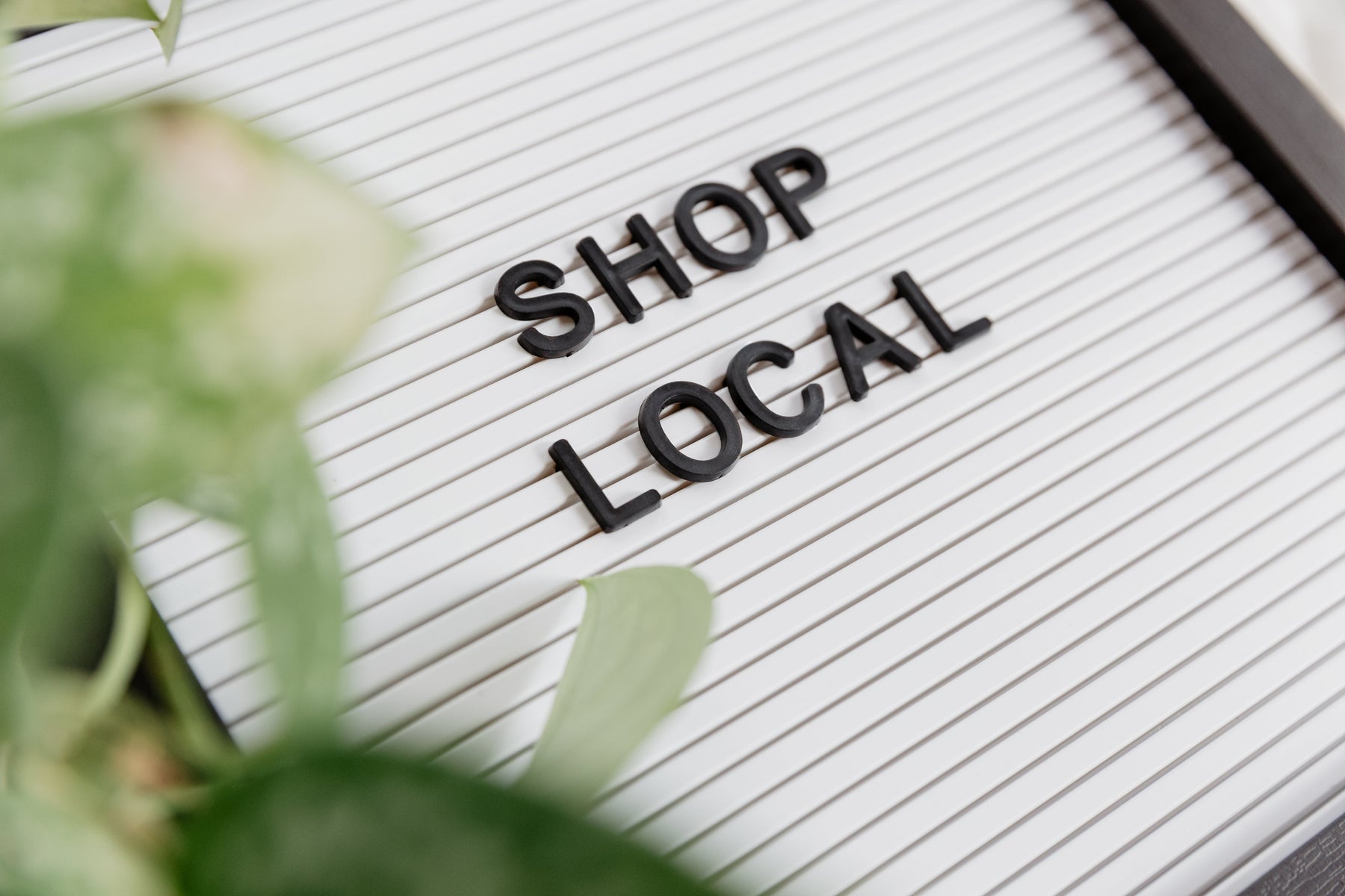 A whiteboard displays Shop Local in the center, as greenery peeks in from the left side of the frame.