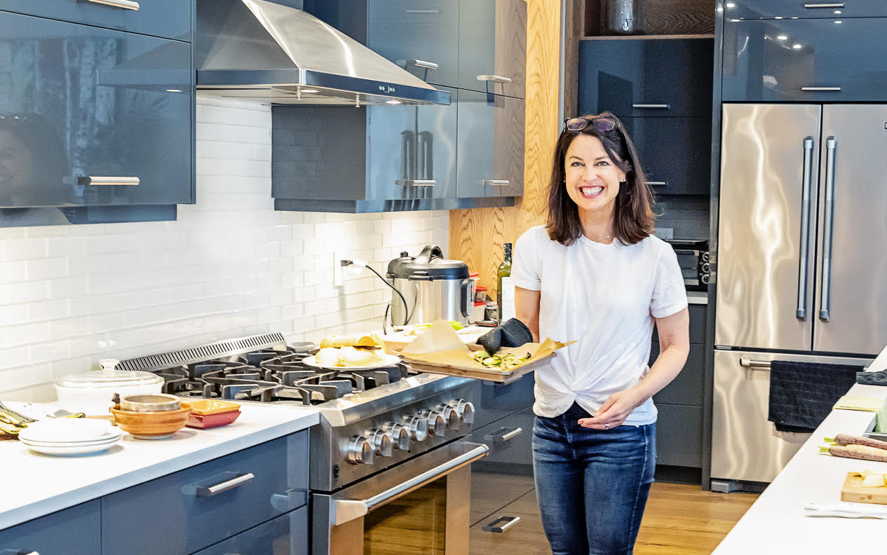 Bonnie Flemington in a large kitchen, smiling and holding a tray of roasted vegetables.