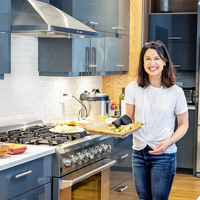 Bonnie Flemington in a large kitchen, smiling and holding a tray of roasted vegetables.