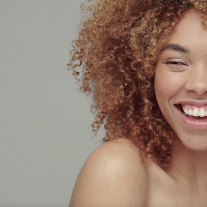 A closeup image of a dark-skinned smiling woman with shoulder-length curly hair and healthy skin 